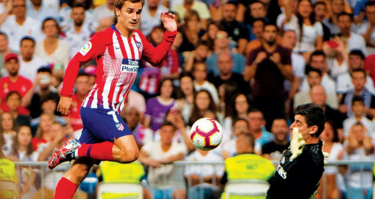 كورتوا حارس ريال مدريد يتصدى لهجمة خطيرة من غريزمان نجم أتلتيكو (أ.ف.ب)