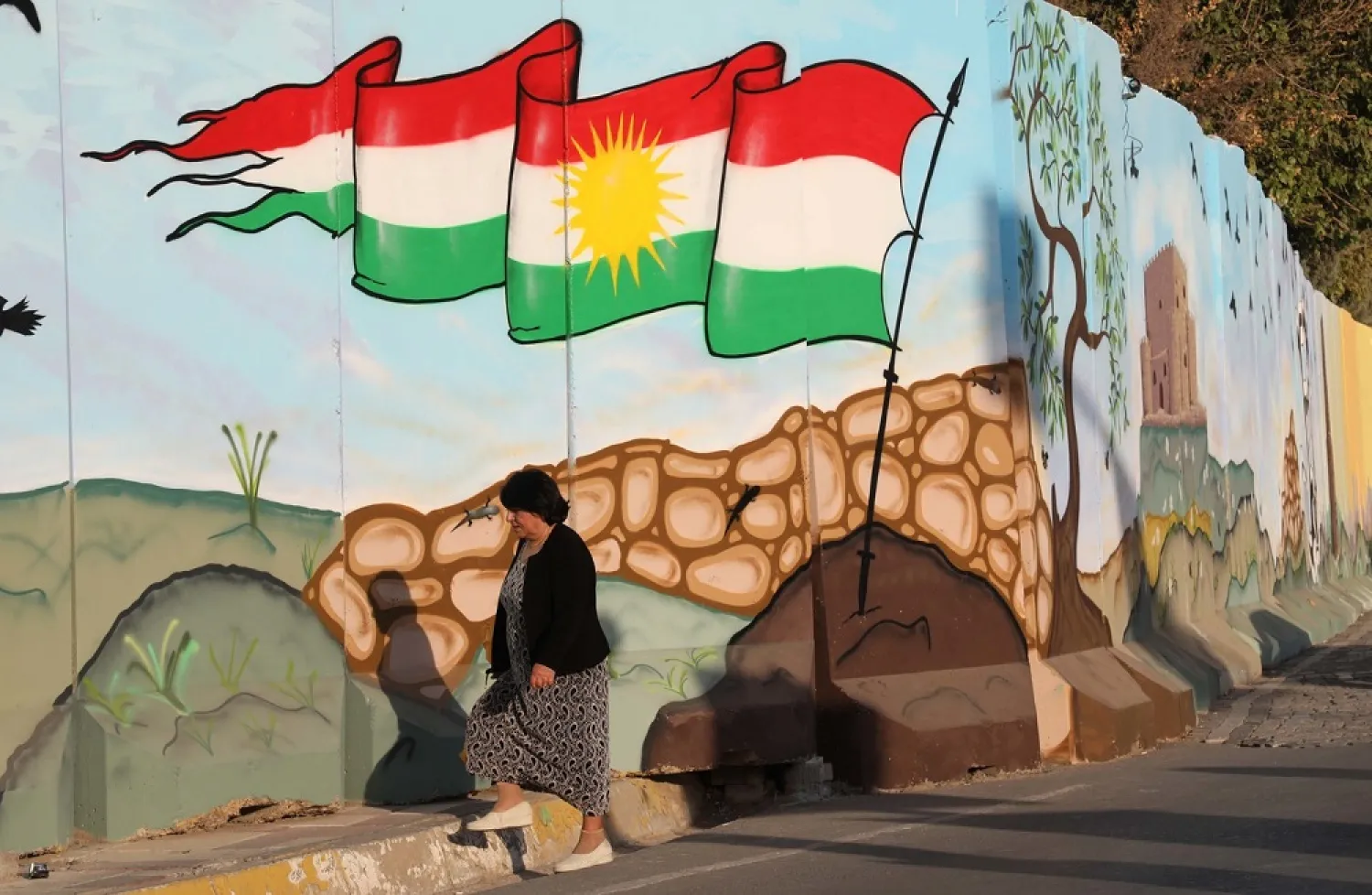 A woman walks passed a mural depicting the Kurdish flag in Erbil. (AFP)
