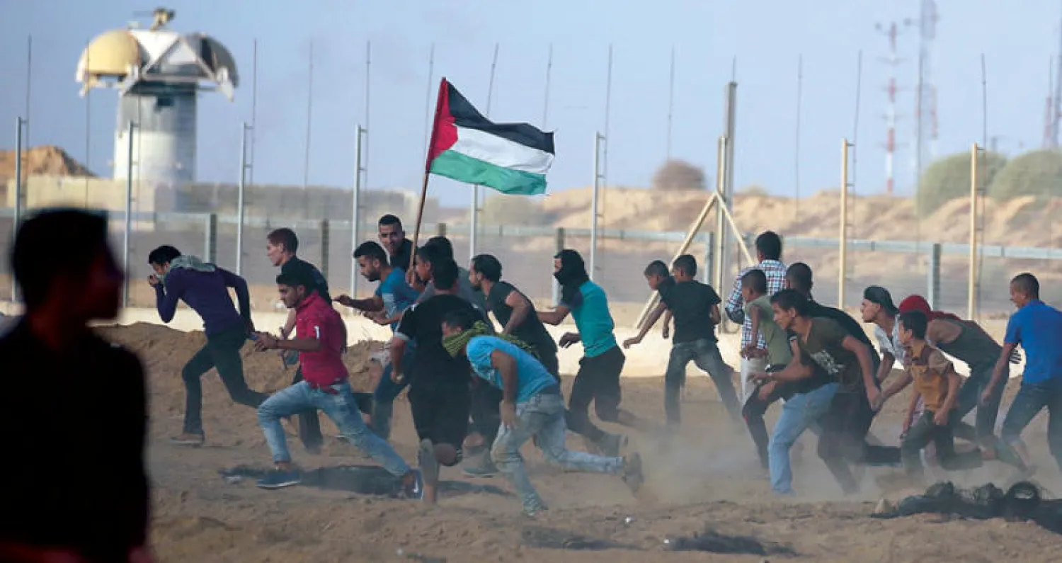 فلسطينيون يحملون علم بلادهم خلال المواجهات التي عرفتها حدود غزة أمس (رويترز)