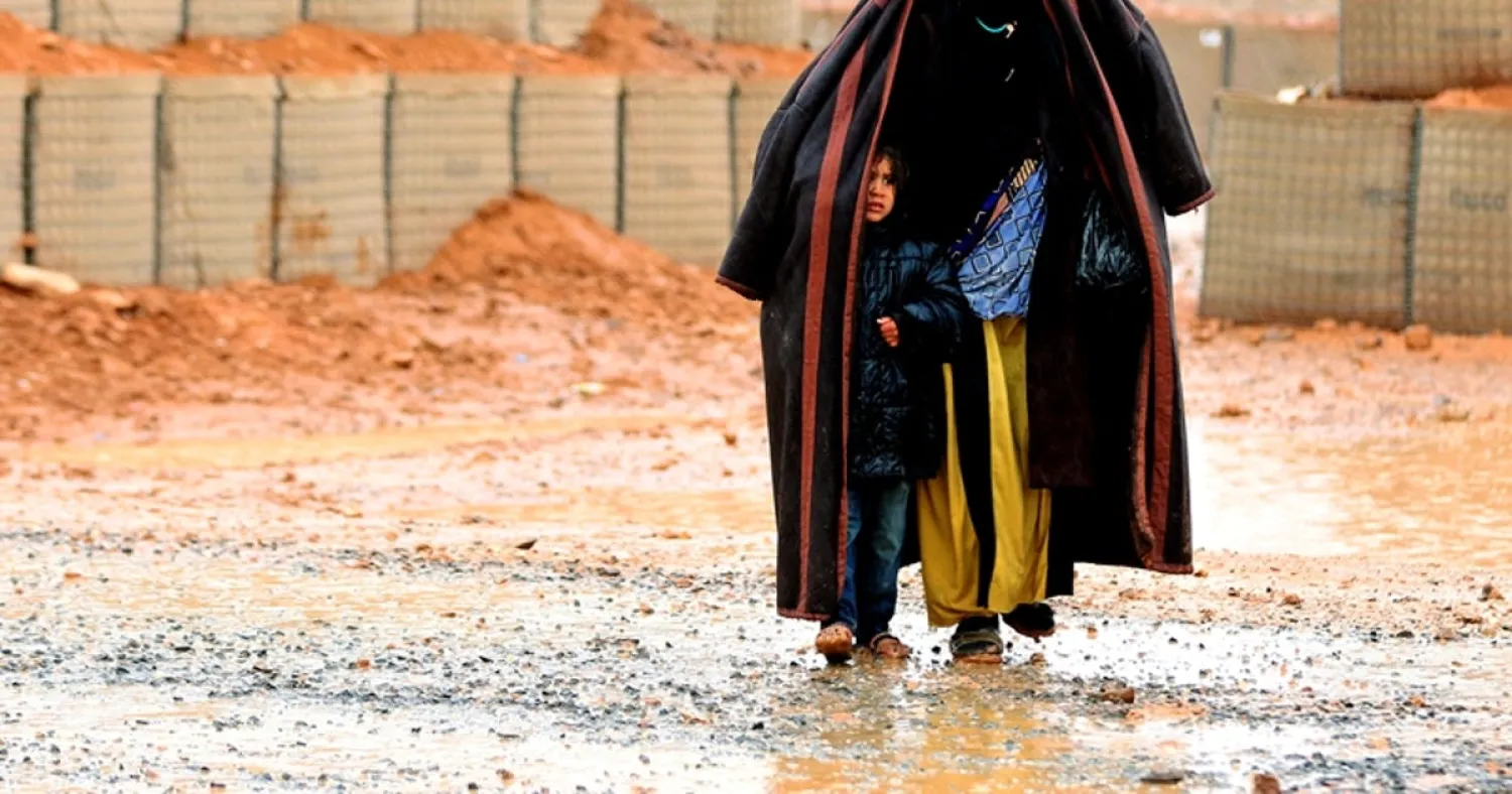 A Syrian refugee from the informal Rukban camp, which lies in no-man's-land off the border between Syria and Jordan in the remote northeast, walks in the rain, as she shelters a young child outside a UN-operated medical clinic immediately on the Jordanian-side on March 1, 2017. KHALIL MAZRAAWI / AFP