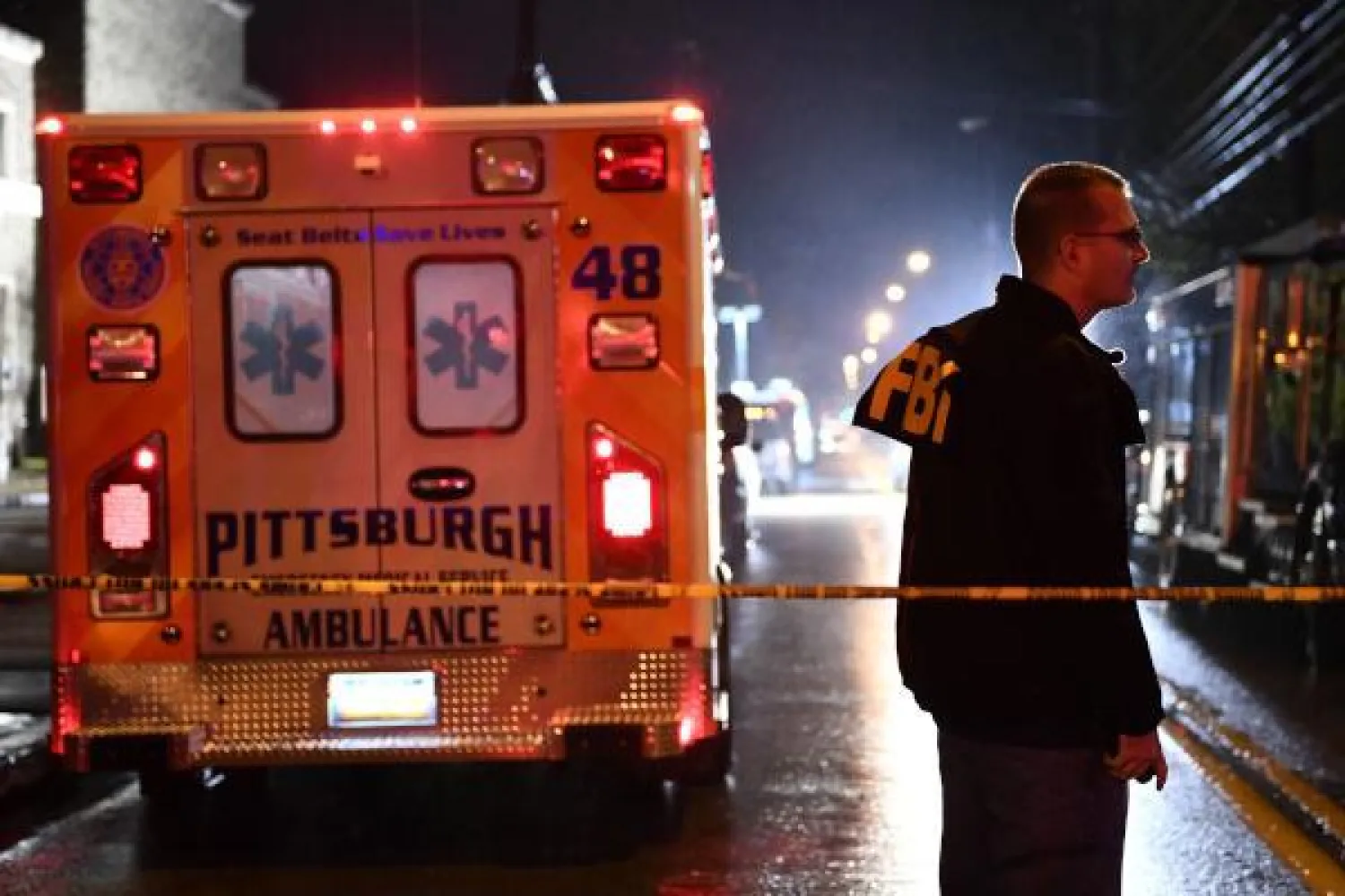 ضابط من مكتب التحقيقات الفيدرالي خلف حاجز أمني وسيارة إسعاف أمام المعبد اليهودي في مدينة بيتسبرغ (ا.ف.ب)