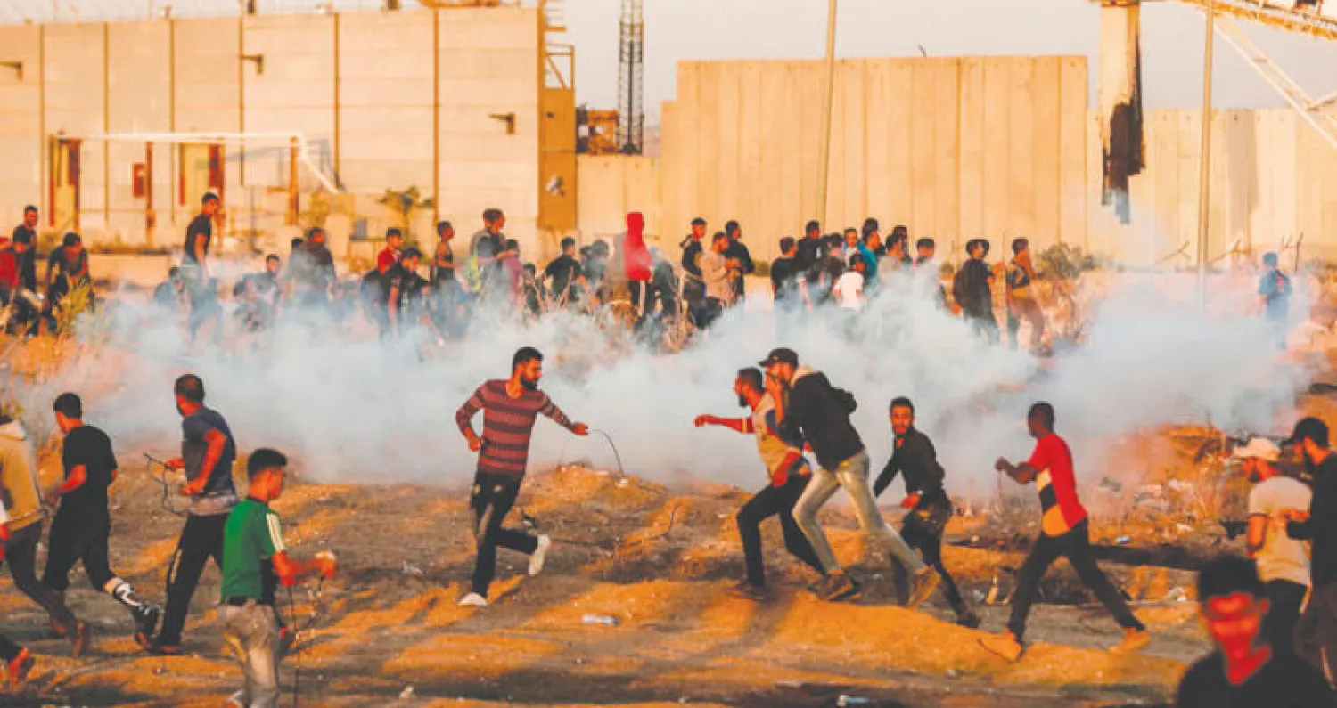 محتجون فلسطينيون يحاولون الاحتماء من قنابل مسيلة للدموع خلال مواجهات مع جنود الاحتلال شرق مدينة غزة أمس (أ.ف.ب)