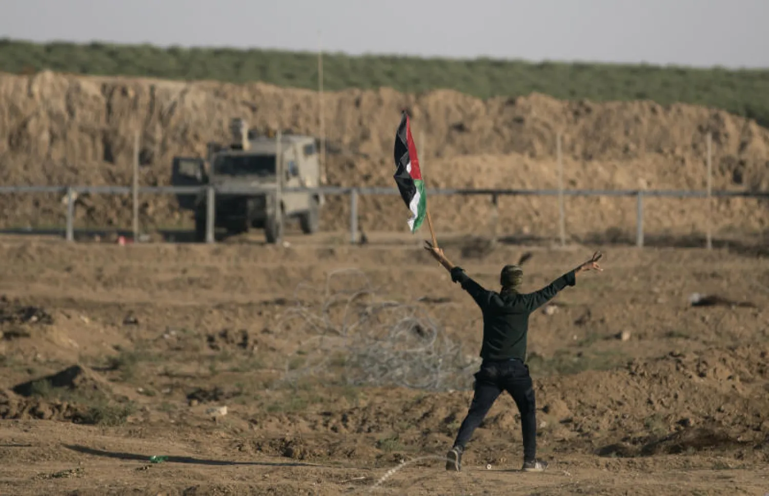 محتج فلسطيني يحمل علم بلاده بالقرب من الحدود في غزة (أ.ب)