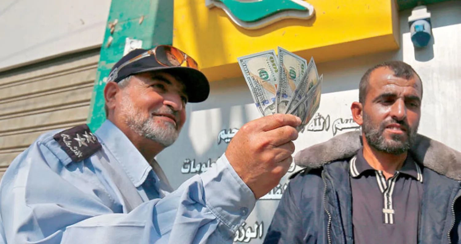 فلسطيني يعرض أوراقاً نقدية بعد تسلمه راتبه في رفح جنوب قطاع غزة أمس (أ.ف.ب)