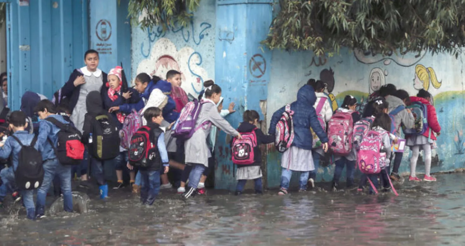 أطفال مدارس يسيرون وسط مياه الفيضانات الناجمة عن الأمطار في غزة أمس (أ.ف.ب)