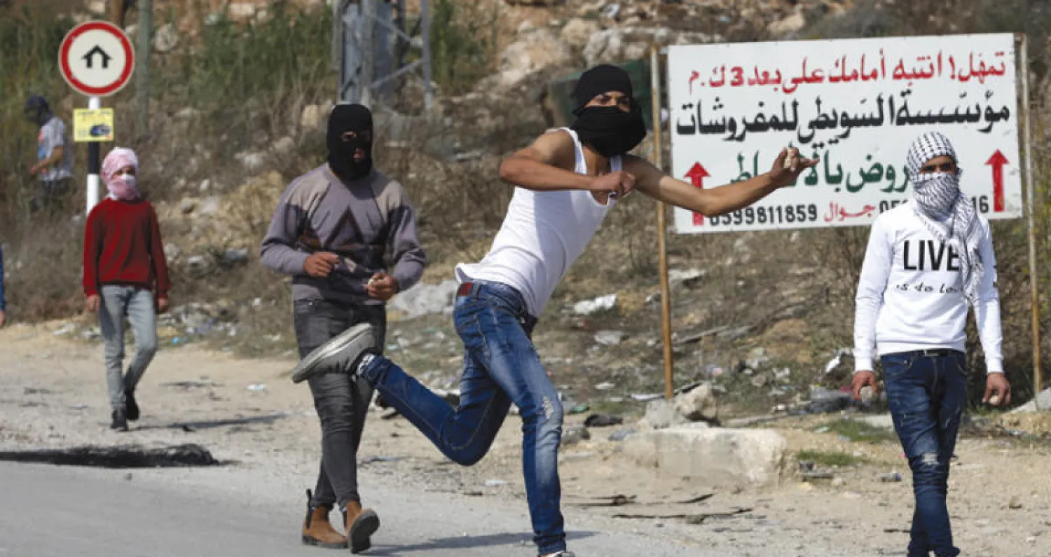 شبان فلسطينيون يلقون الحجارة على قوات الاحتلال خلال اشتباكات في قرية دورا قرب الخليل (إ.ب.أ)