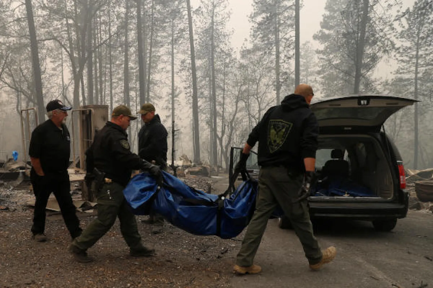 رجال شرطة ينقلون جثة خلال تمشيط مخيم التهمته النيران في باراديز (رويترز)
