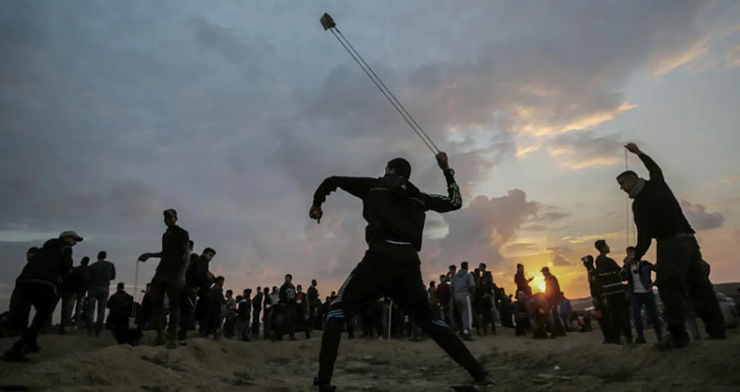 شبان فلسطينيون يرشقون الجيش الإسرائيلي بالحجارة على حدود غزة (إ.ب.أ)