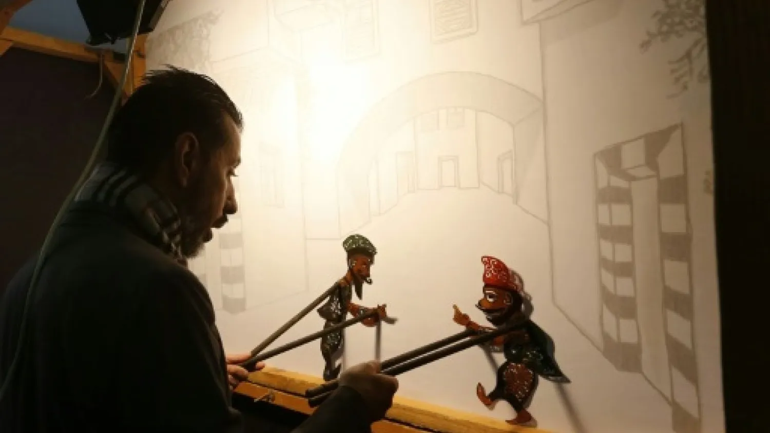 Syria's last shadow puppeteer Shadi al-Hallaq is seen moving his puppets Karakoz (R) and Eiwaz (L) from inside his booth during a presentation in Damascus | AFP