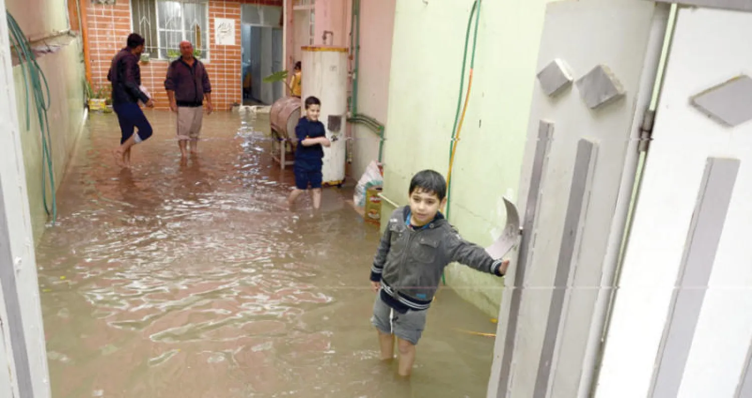 عراقي مع أولاده وسط مياه السيول التي غمرت منزلهم في الموصل (إ.ب.أ)