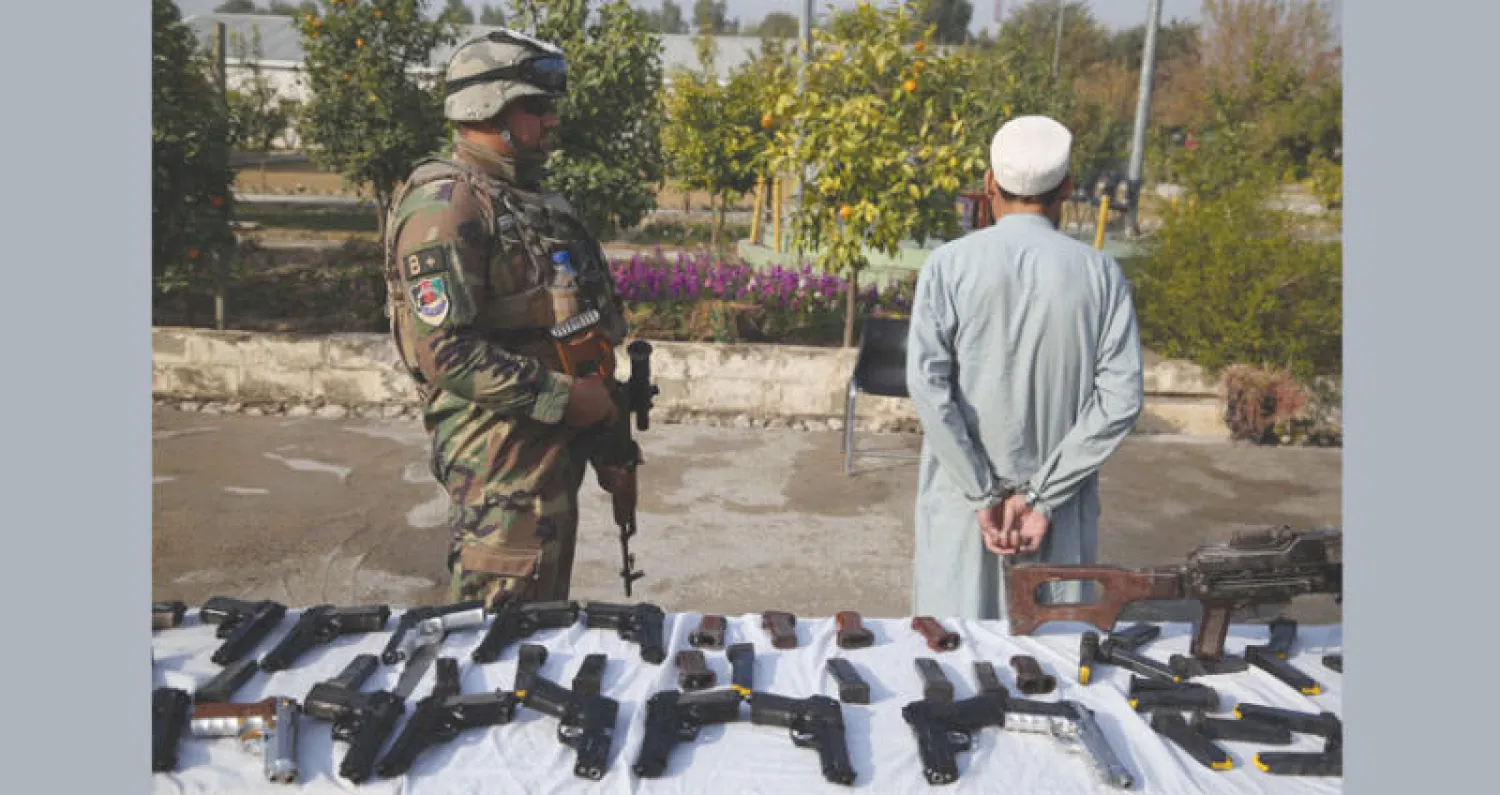 أحد عناصر حركة {طالبان} بعد اعتقاله في جلال آباد وخلفه أسلحة مصادرة (إ.ب.أ)