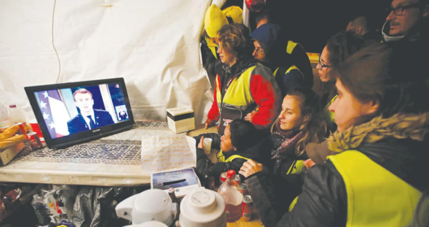 متظاهرون من «السترات الصفراء» يتابعون خطاب ماكرون قرب مدينة مرسيليا أمس (رويترز)