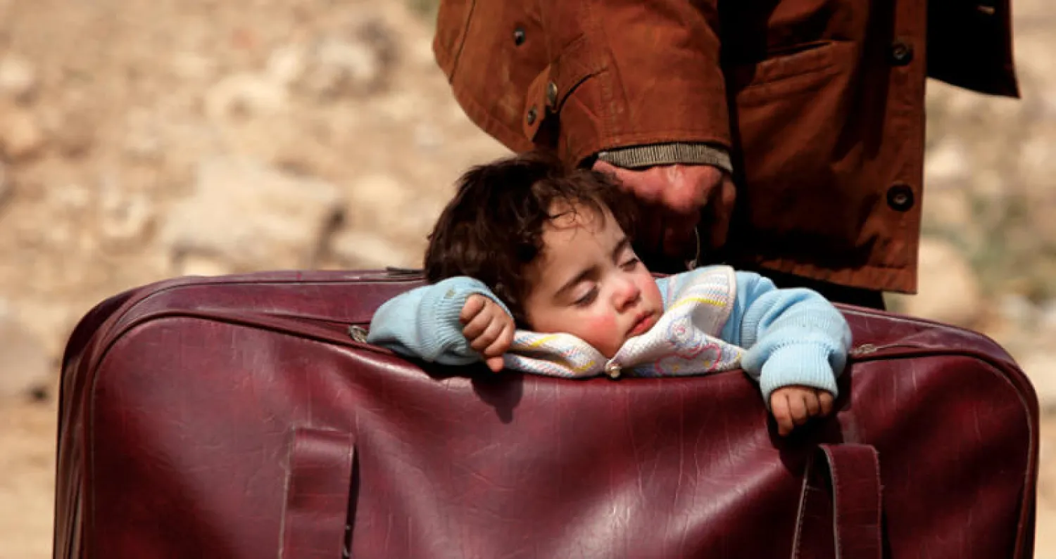 صورة ارشيفية لطفل نازح يحمله والده في حقيبة سفر (رويترز)