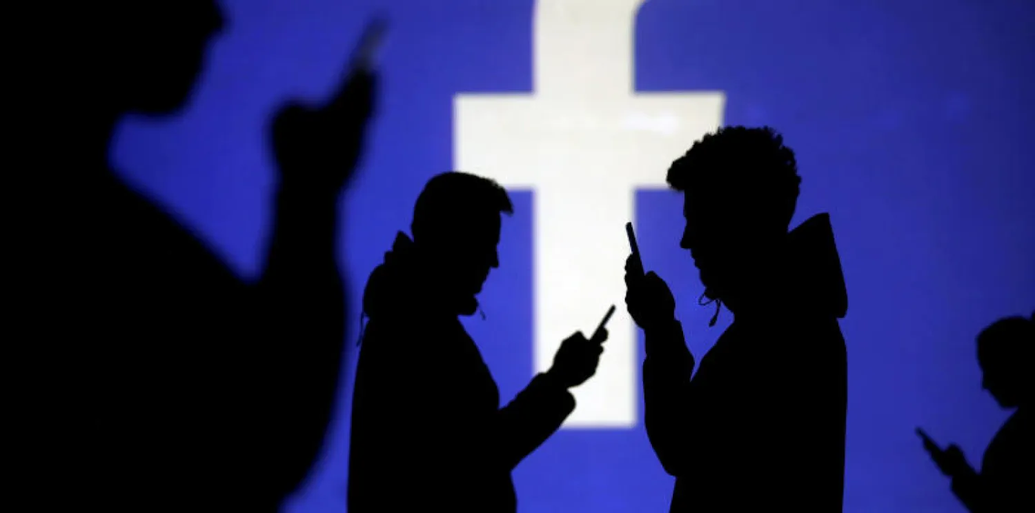 صورة تظهر ظلاً لمستخدمي الهواتف الجوالة بجوار شاشة تعرض شعار «فيسبوك» (رويترز)