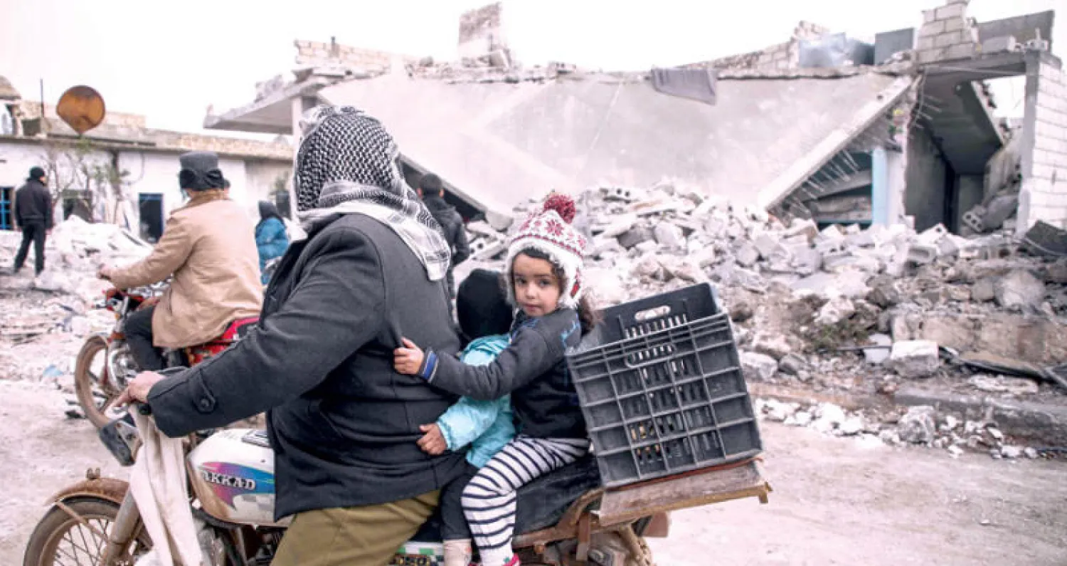 سوري مع ولديه على دراجة نارية قرب مبنى دمرته غارة جوية للنظام في أورم الكبرى بريف حلب أمس (أ.ف.ب)