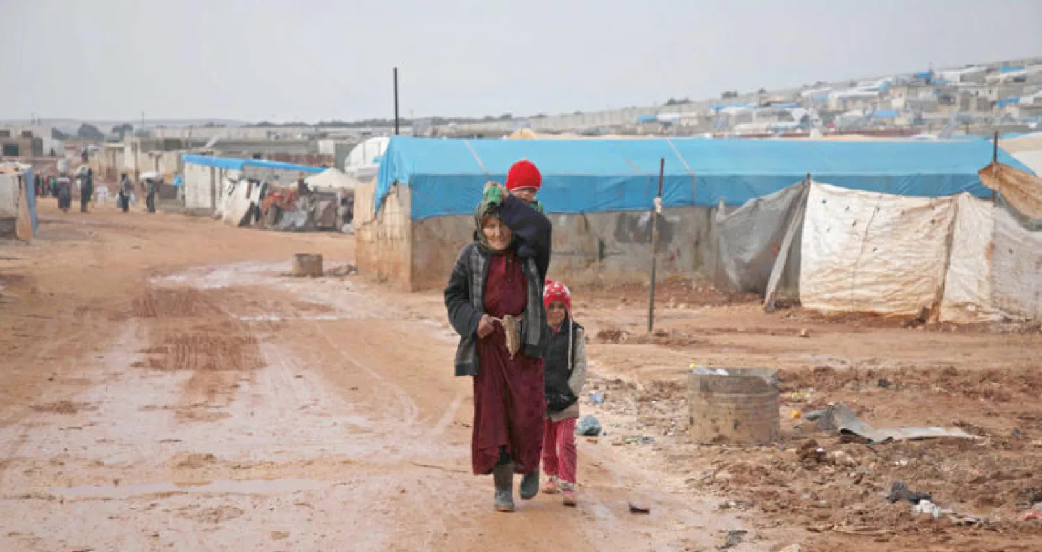 نازحة سورية مع طفليها وسط الوحل شمال البلاد أمس (أ.ف.ب)