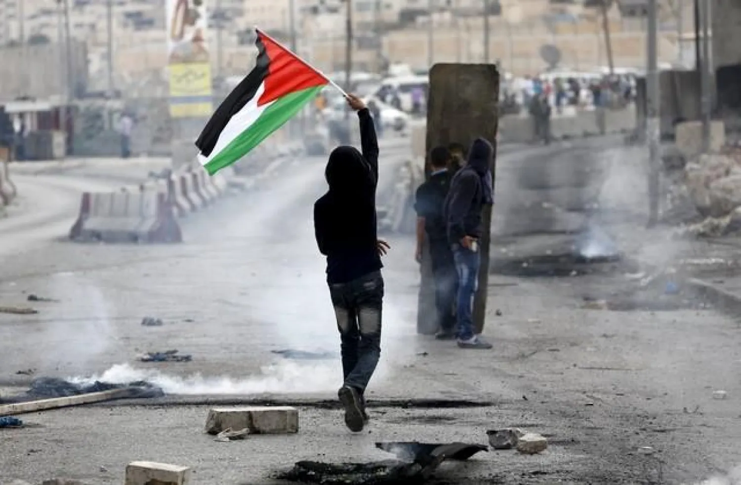 A Palestinian protester holds a Palestinian flag as others take cover during clashes with the Israeli army at Qalandia checkpoint near occupied West Bank city of Ramallah (File Photo: Reuters)