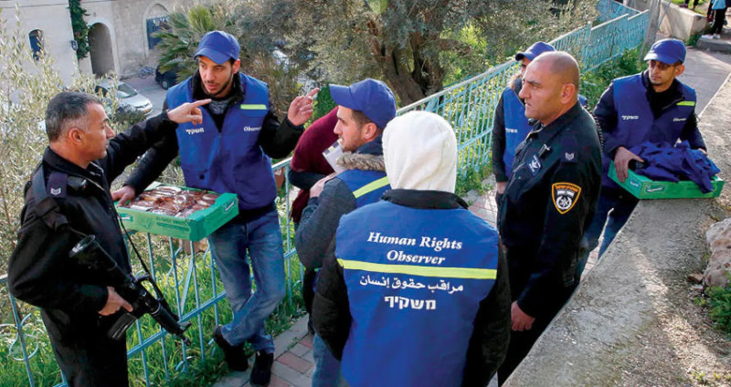 رجل شرطة إسرائيلي يتحدث إلى ناشطي حقوق إنسان فلسطينيين قرب شارع «الشهداء» في الخليل أمس (أ.ف.ب)