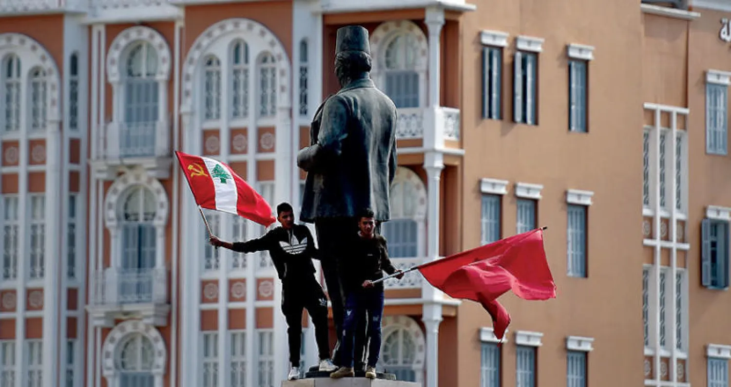 متظاهران تسلقا تمثال رياض الصلح وسط بيروت خلال تجمع لـ«الشيوعي» اللبناني احتجاجاً على الأوضاع المعيشية (إ.ب.أ)