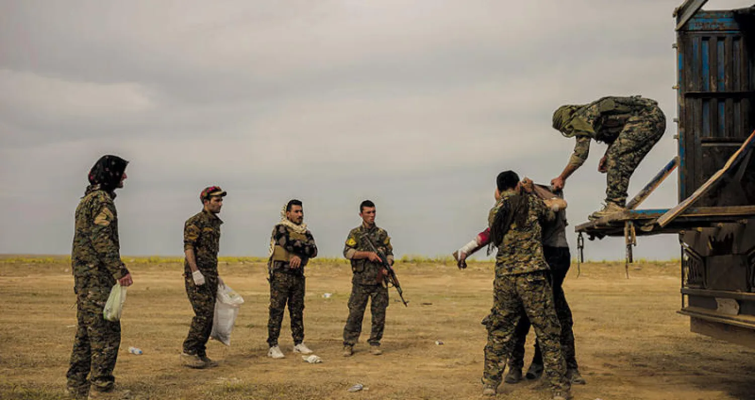 عناصر من «قوات سوريا الديمقراطية» يساعدون جرحى قرب الباغوز (أ.ب)