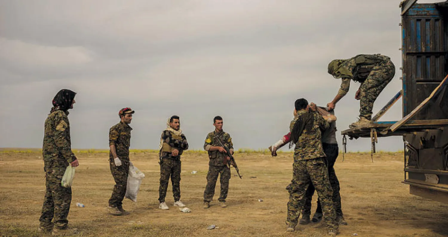 عناصر من «قوات سوريا الديمقراطية» يساعدون جرحى قرب الباغوز (أ.ب)