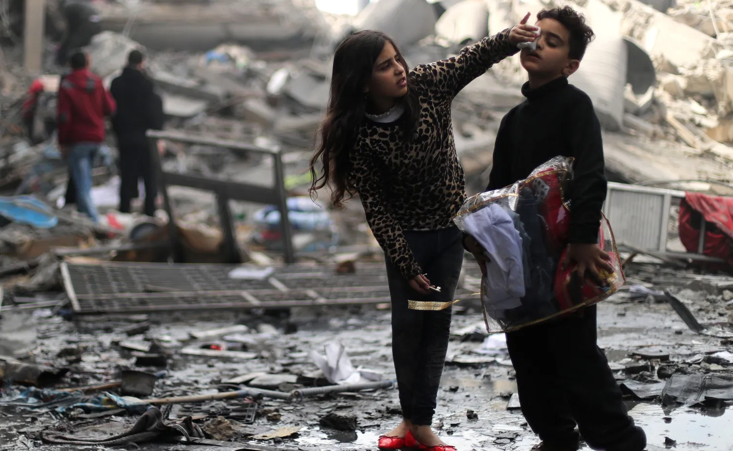 فتاة فلسطينية تنظّف وجه شقيقها فوق بقايا منزلهما المدمّر بالقصف الإسرائيلي في مدينة غزة (رويترز)