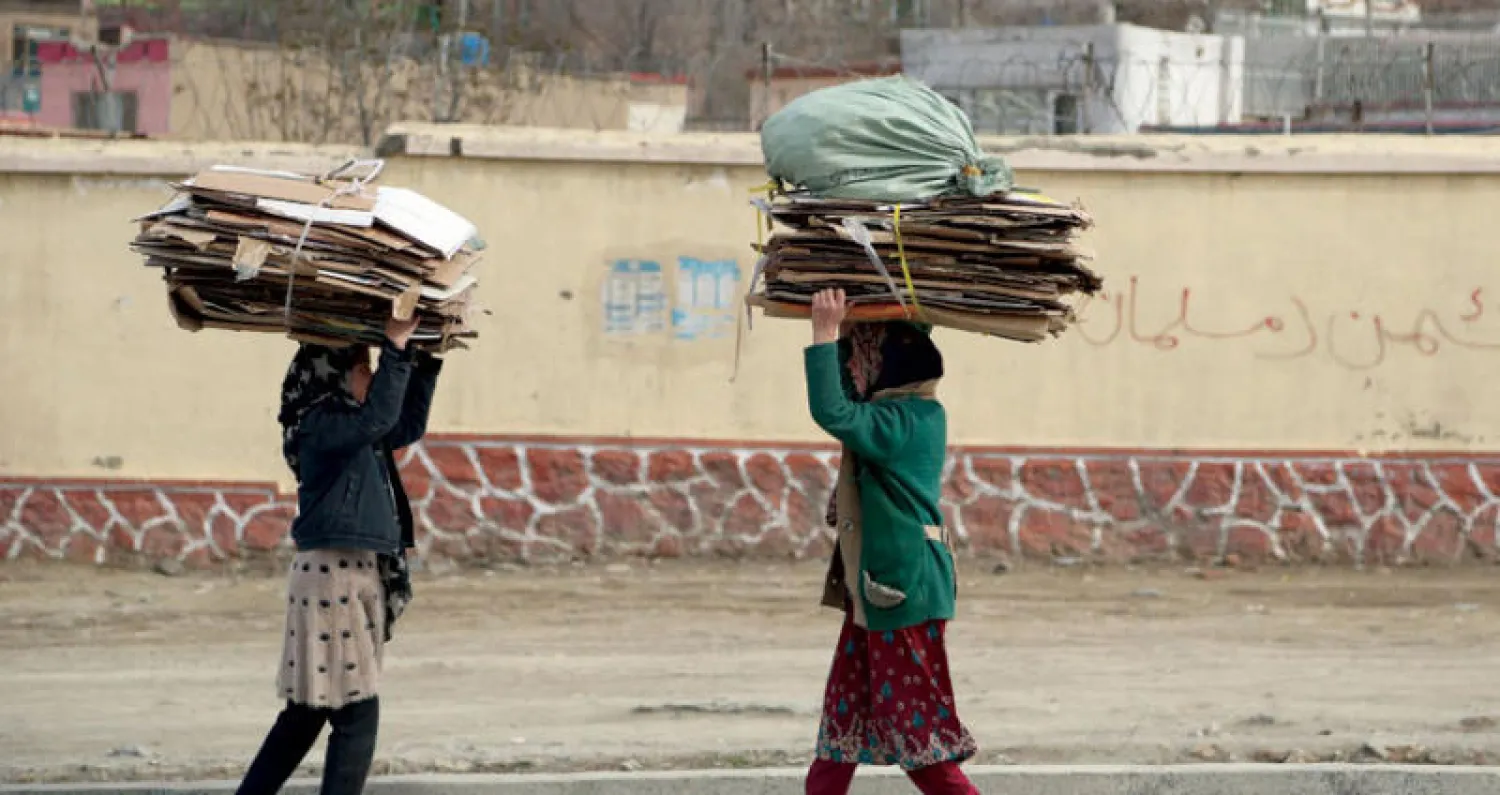 صبيتان تحملان أول من أمس كراتين مطوية للاستخدام في التدفئة عوضاً عن الحطب في كابل (أ.ب)