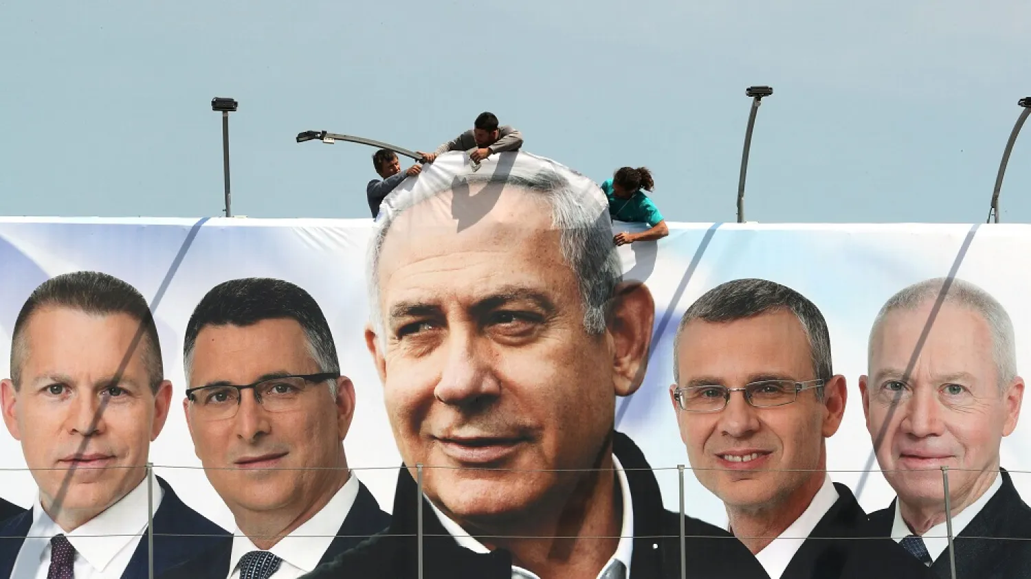 Laborers hang a Likud election campaign banner depicting Israeli Prime Minister Benjamin Netanyahu with Likud candidates, in Jerusalem, March 28, 2019. (Reuters)