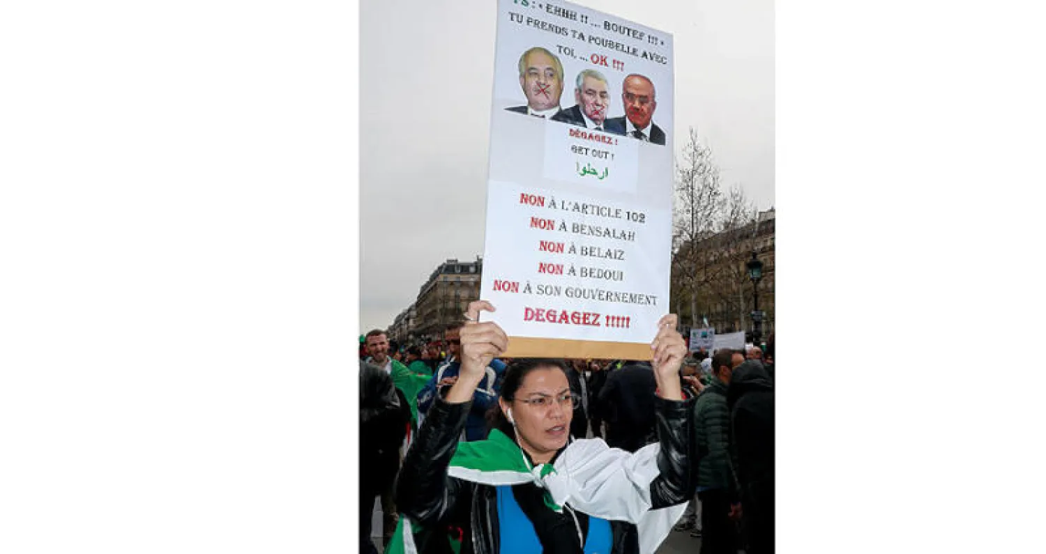 إمرأة ترفع شعاراً خلال تظاهرة جزائرية في باريس يوم الأحد للمطالبة بتنحي رئيس مجلس الأمة ورئيس المجلس الدستوري ورئيس الحكومة خلال المرحلة الانتقالية (أ.ف.ب)
