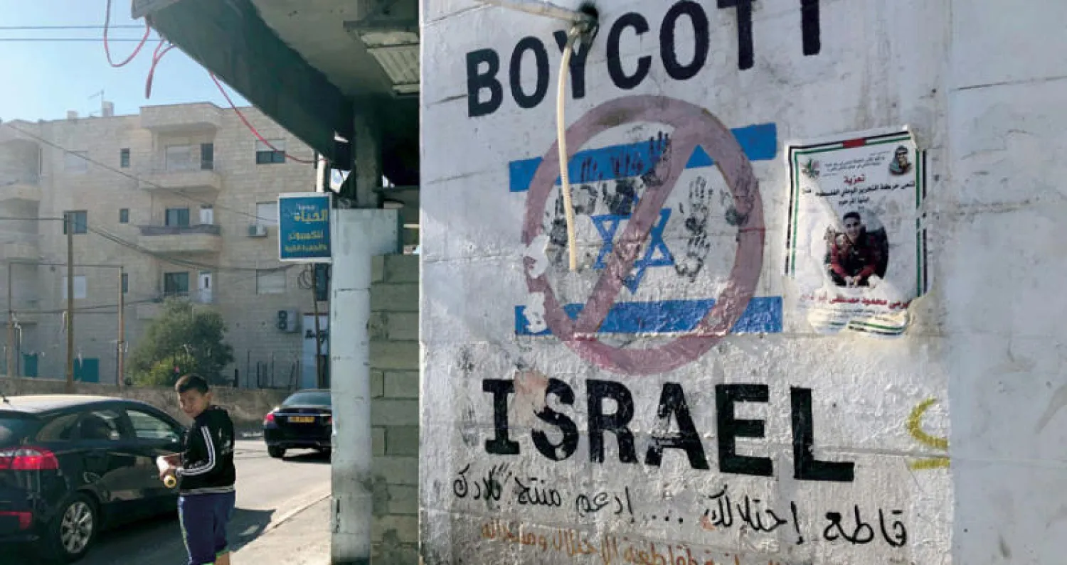 صبي فلسطيني من بيت لحم في الضفة الغربية يقرأ دعوة لمقاطعة إسرائيل في نوفمبر الماضي (رويترز)