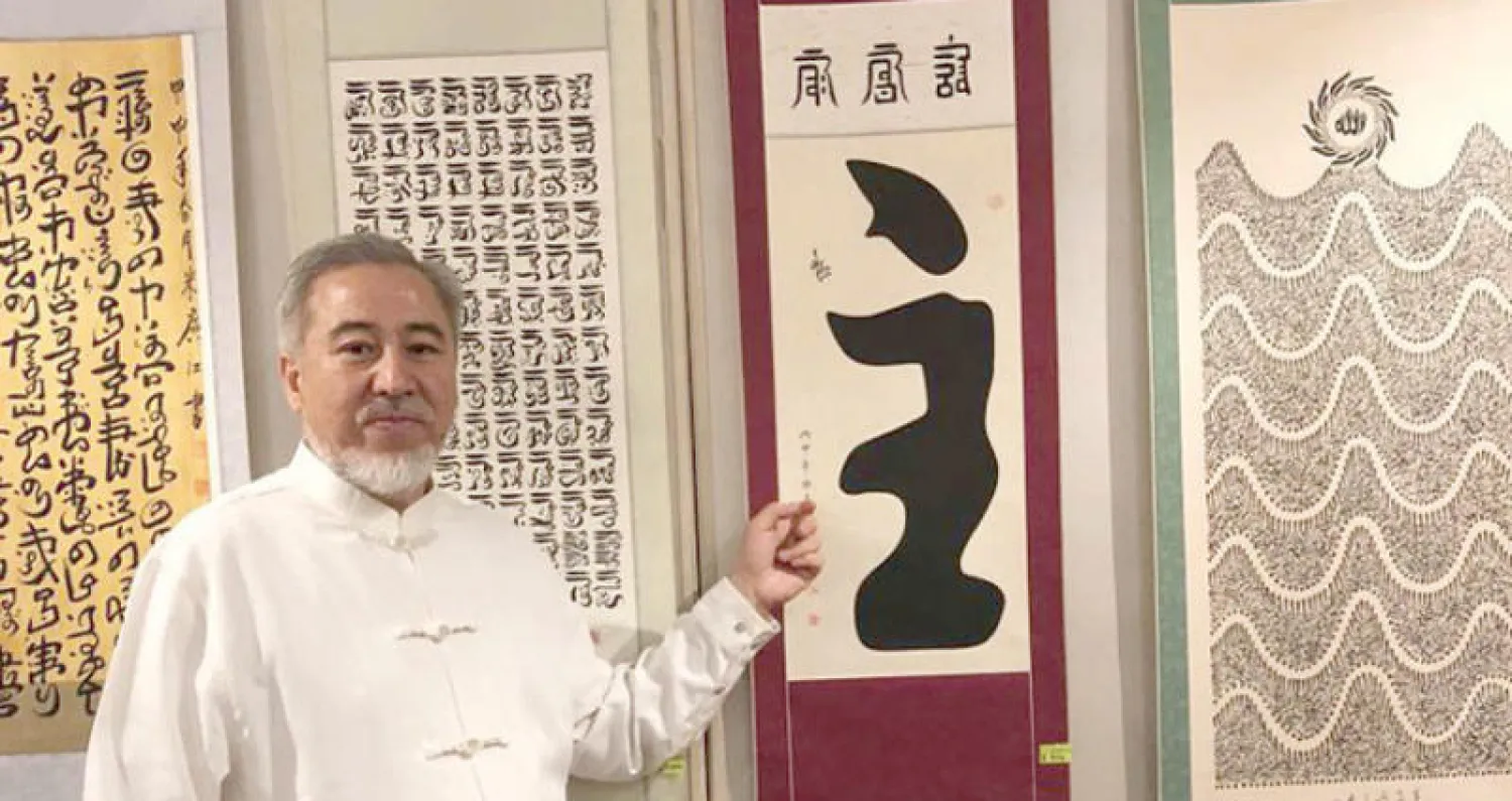 الخطاط الصيني الحاج نور الدين أمام إحدى اللوحات وكتب فيها لفظ الجلالة الله بحيث يقرأ باللغتين العربية والصينية