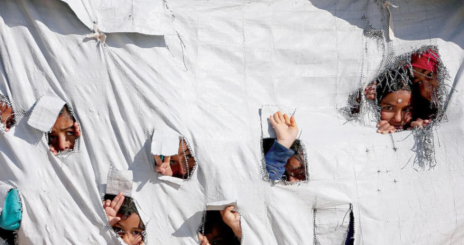 أطفال ينظرون من خيمة في مخيم الهول شرق سوريا أمس (رويترز)