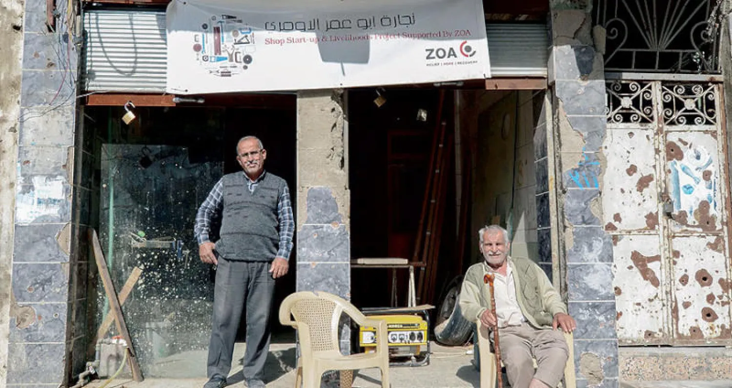 عراقيان أمام متجرهما الذي تبدو عليه آثار الخراب مما حل في الموصل من معارك سابقة (أ.ف.ب)