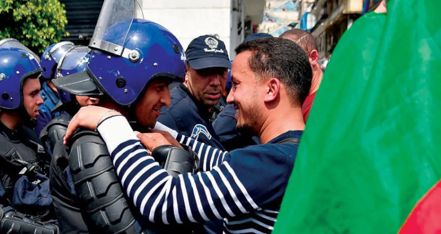 عناق بين متظاهر جزائري وأحد عناصر قوات الأمن خلال المظاهرات التي شهدتها شوارع العاصمة أمس (أ.ف.ب)