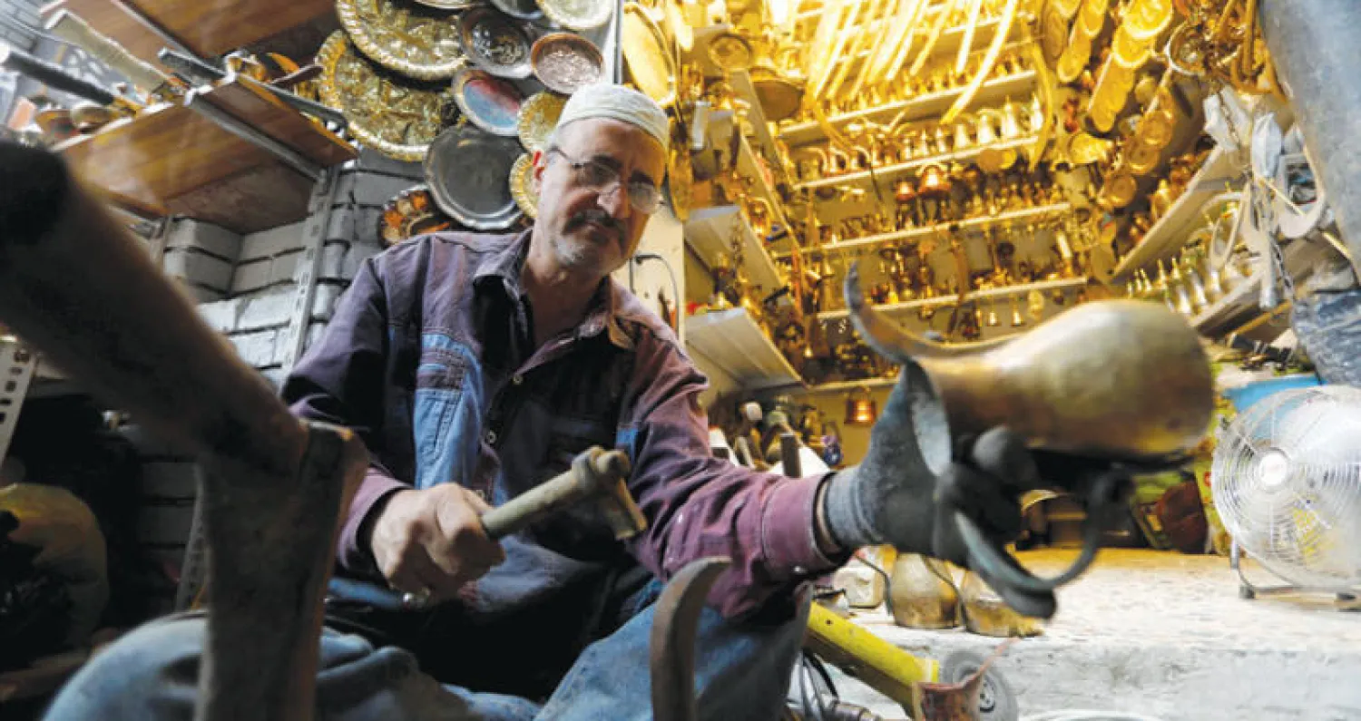 بائع يعمل على قطعة من النحاسيات في بغداد (رويترز)