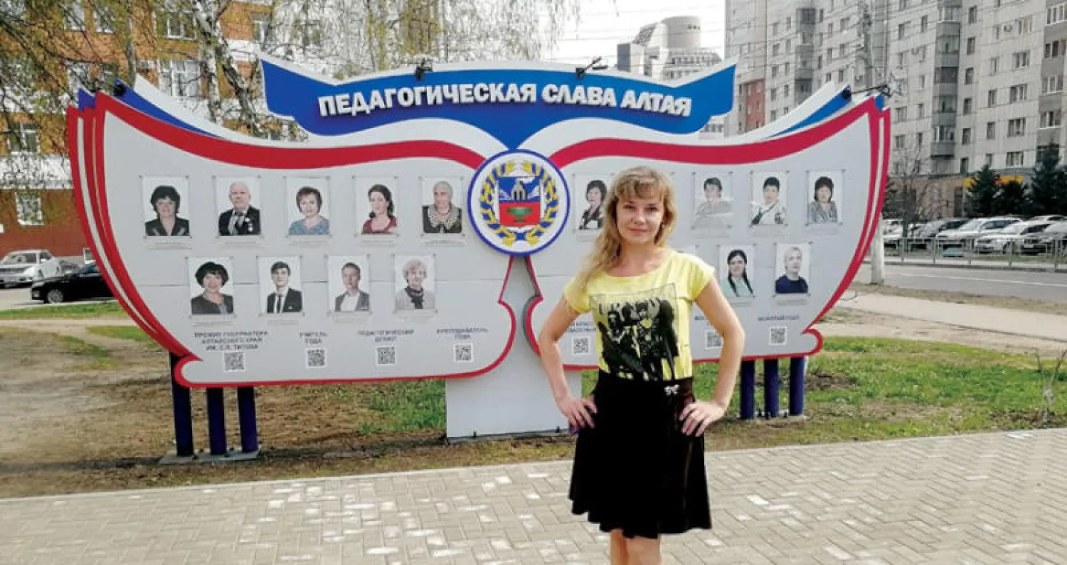 المعلمة تتيانا وخلفها لوحة أفضل المعلمين في إقليم ألتاي