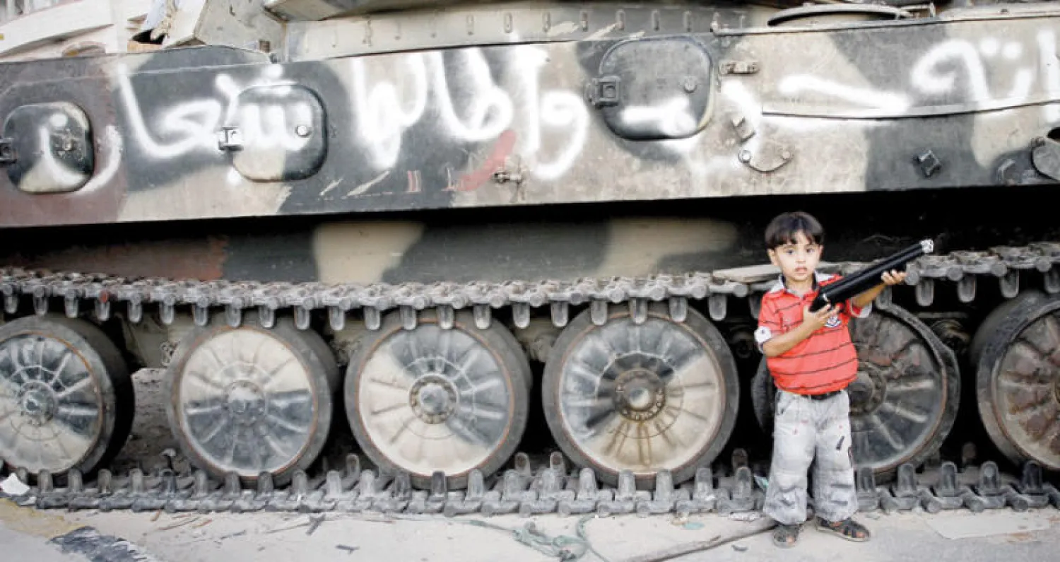 طفل يقف أمام دبابة في مدينة مصراتة التي شيعت قبل أيام جثامين 3 أطفال كانوا يقاتلون مع الميليشيات المسلحة (غيتي)