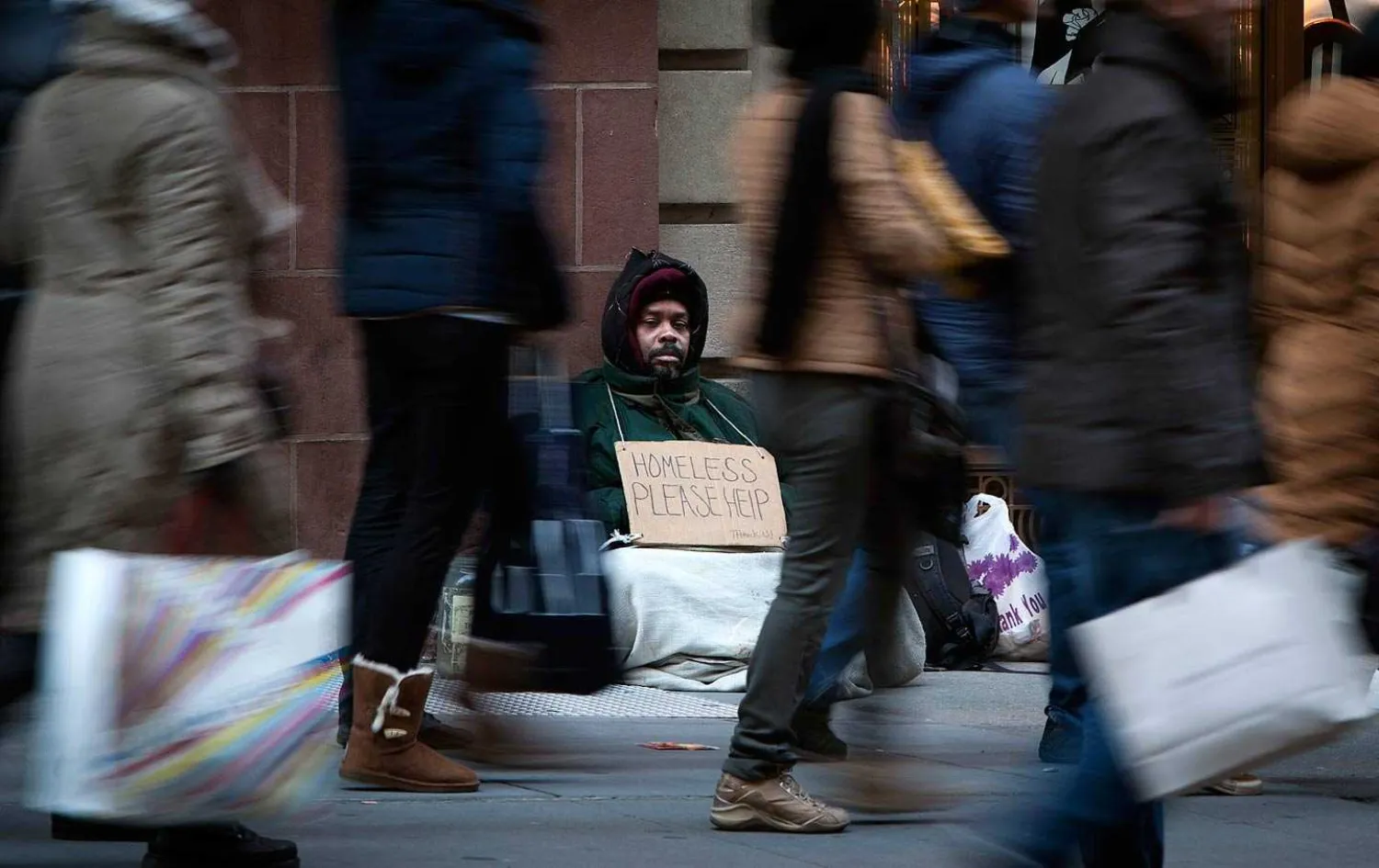 A man who says he is homeless sits on Fifth Avenue in Manhattan as shoppers pass, looking for Black Friday sales, November 29, 2013. (Reuters / Carlo Allegri)