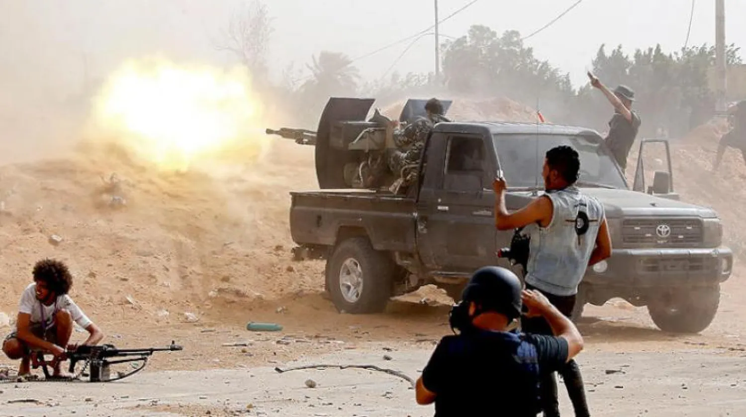 A fighter loyal to the GNA fires a heavy machine gun as a press photographer take pictures of the scene during clashes with the LNA, on May 25, 2019, in the Airport Road Area, south of the Libyan capital Tripoli. 
Mahmud TURKIA / AFP