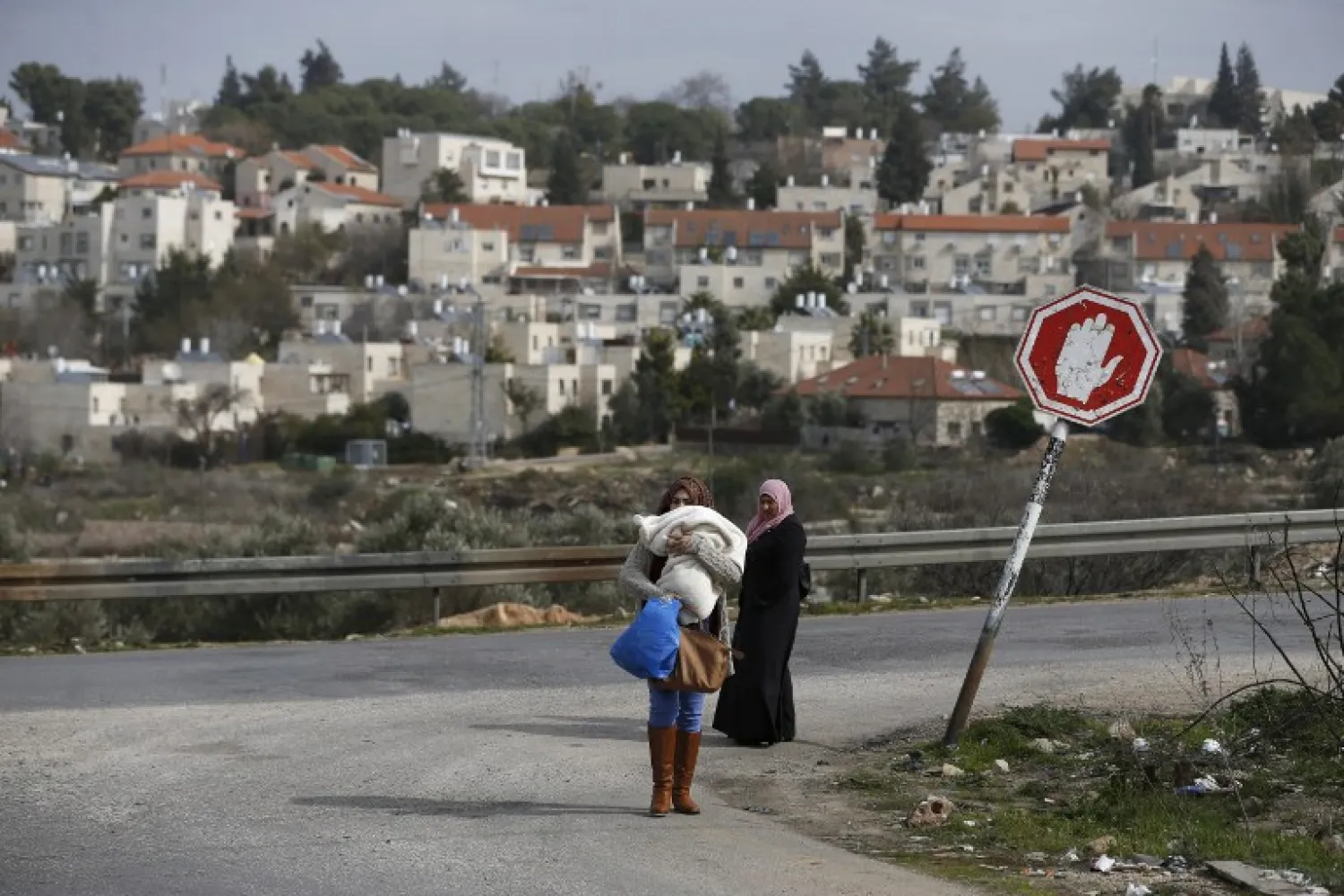 Palestinian women from the Jalazoun refugee camp stand at a crossroad in the West Bank city of Ramallah with the Israeli settlement of Beit El seen behind them, (File Photo: AFP)
