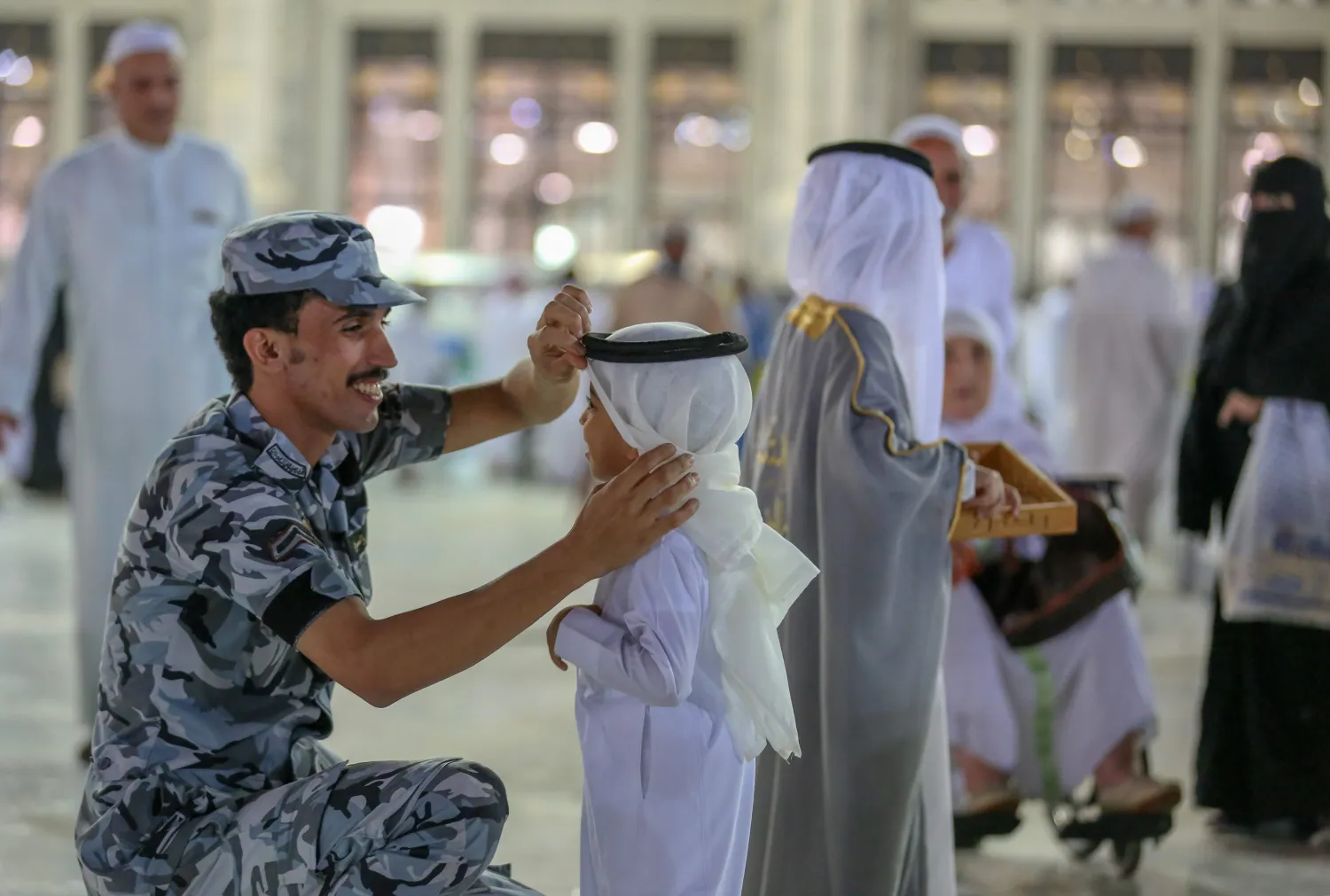 فرد أمن سعودي يصلح وشاح الرأس لطفل بعد صلاة عيد الفطر في المسجد الحرام (أ.ف.ب)