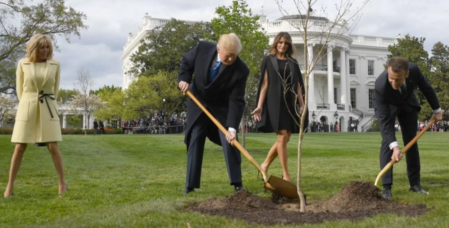 الرئيس الفرنسي إيمانويل ماكرون والرئيس الأميركي دونالد ترمب يزرعان شجرة الصداقة وخلفهما ميلانيا ترمب وبريغيت ماكرون (أ.ف.ب)