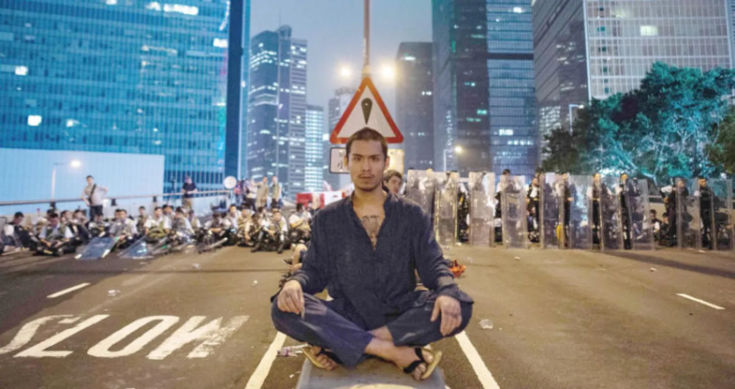 متظاهر يجلس أمام متظاهرين ورجال أمن عقب يوم من المواجهات في هونغ كونغ الأربعاء (أ.ف.ب)