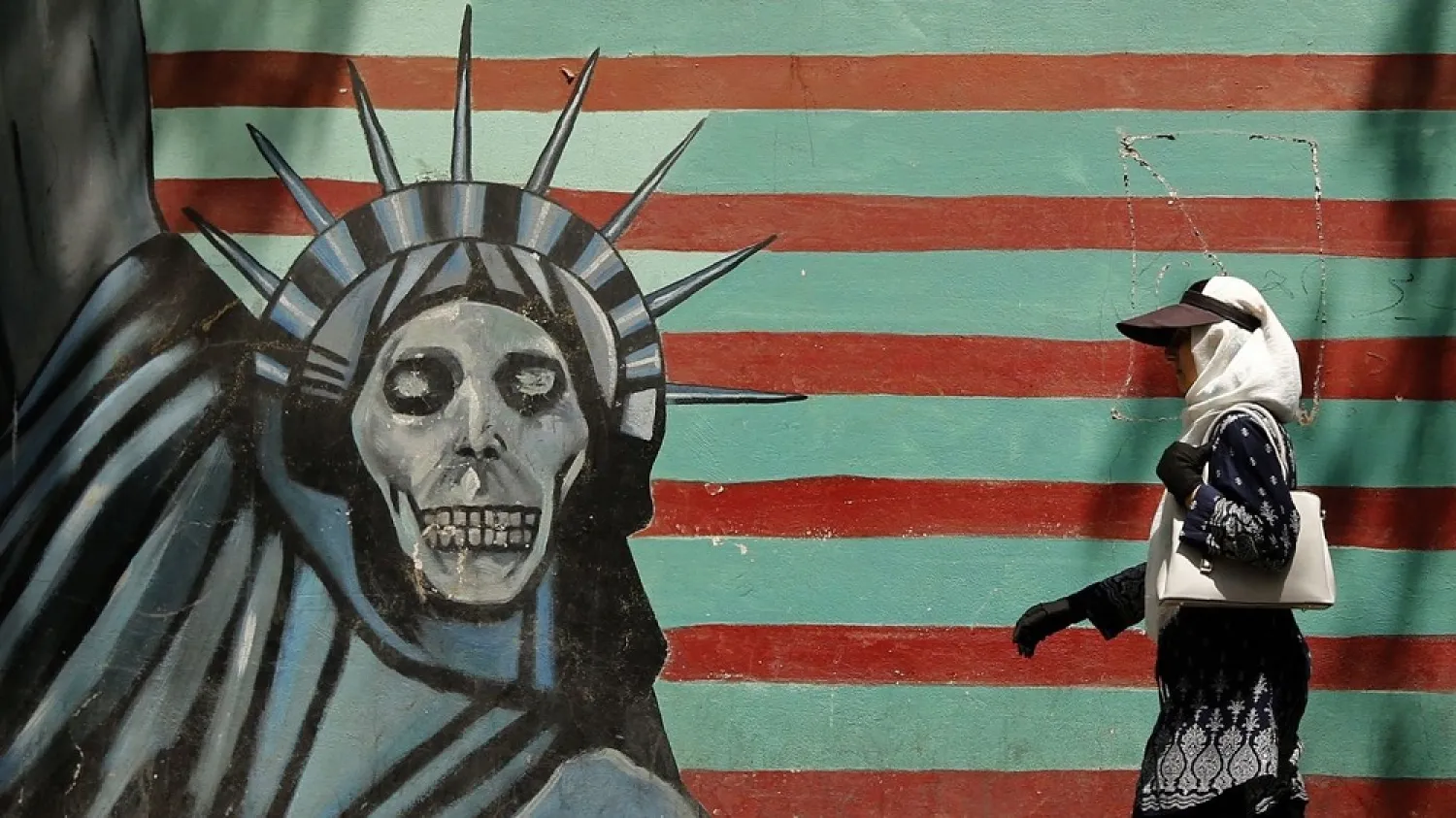 An Iranian woman walks past the former US Embassy in Tehran, which bears a mural depicting the Statue of Liberty with a dead face. (Getty Images)