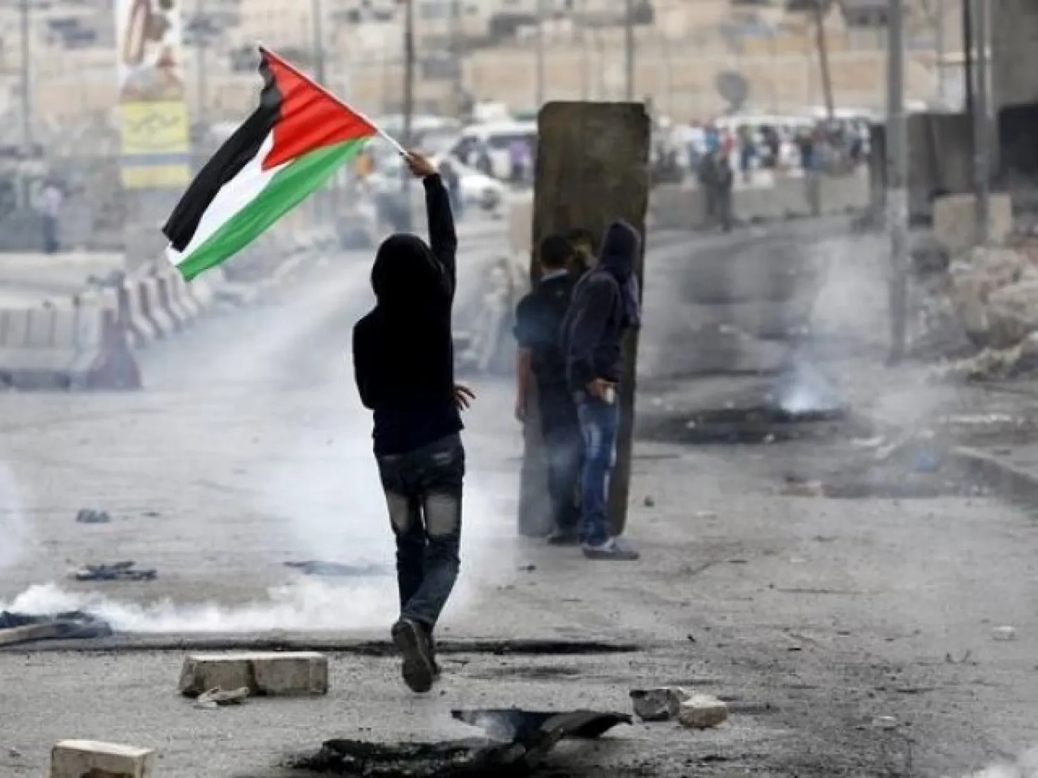 A Palestinian protester holds a Palestinian flag as others take cover during clashes with the Israeli army at Qalandia checkpoint near occupied West Bank city of Ramallah, October 6, 2015. PHOTO: REUTERS