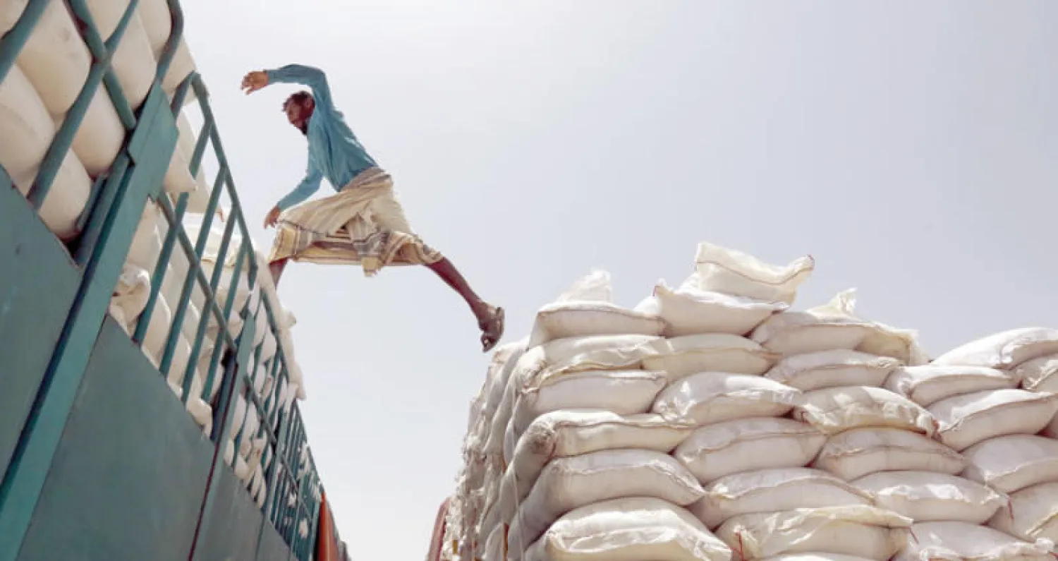 عامل يقفز من شاحنة تحمل دقيقاً مقدماً من برنامج الغذاء العالمي الذي أوقف جزئياً أعماله في صنعاء بسبب رفض الحوثيين نظام البصمة للتأكد من التوزيع (إ.ب.أ)