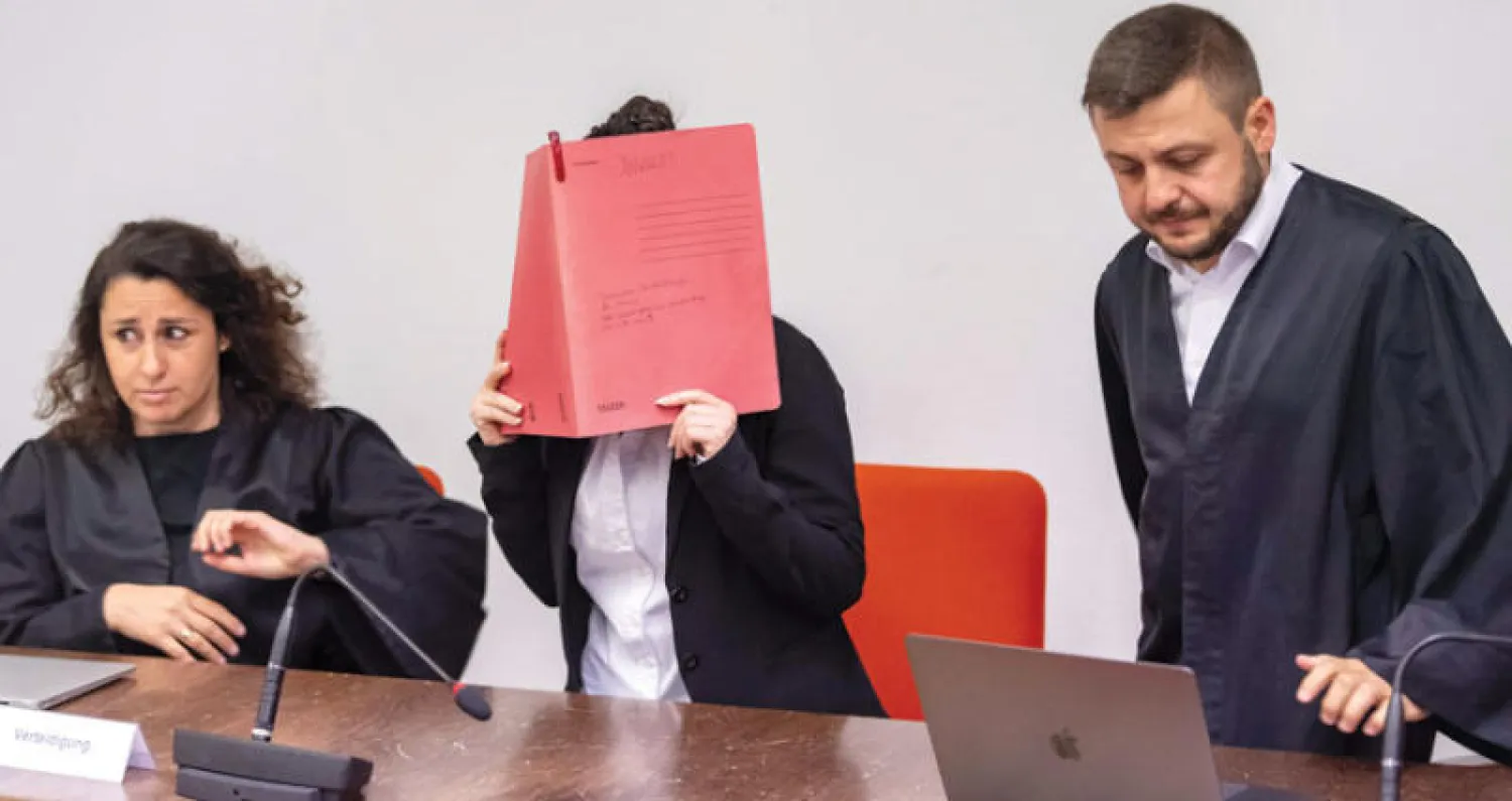 جنيفر المتهمة الألمانية بالانتماء إلى «داعش» (وسط) تخفي وجهها بكتاب لدى مثولها أمام محكمة ميونيخ أمس (أ.ف.ب)