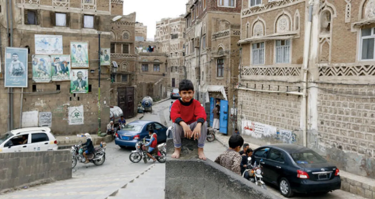 طفل يمني يجلس ومن خلفه مبان في صنعاء القديمة امتلأت بصور قتلى الحوثيين (إ.ب.أ)