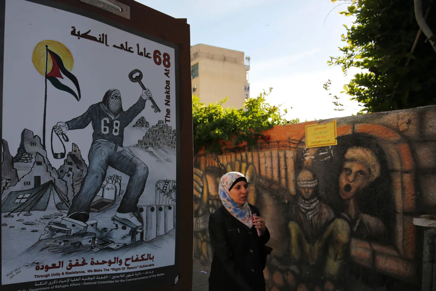 A Palestinian woman walks past a poster depicting a key symbolizing the keys to houses left by Palestinians in 1948, on May 11, 2016, in the West Bank city of Ramallah. (AFP)