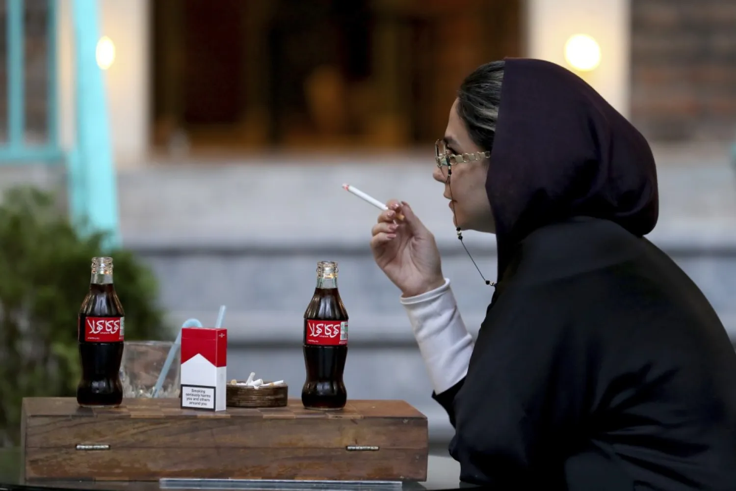 An Iranian smokes a Marlboro cigarette while two Coca-Cola stand on her table at a cafe in downtown Tehran, Iran, Wednesday, July 10, 2019. (AP Photo/Ebrahim Noroozi)